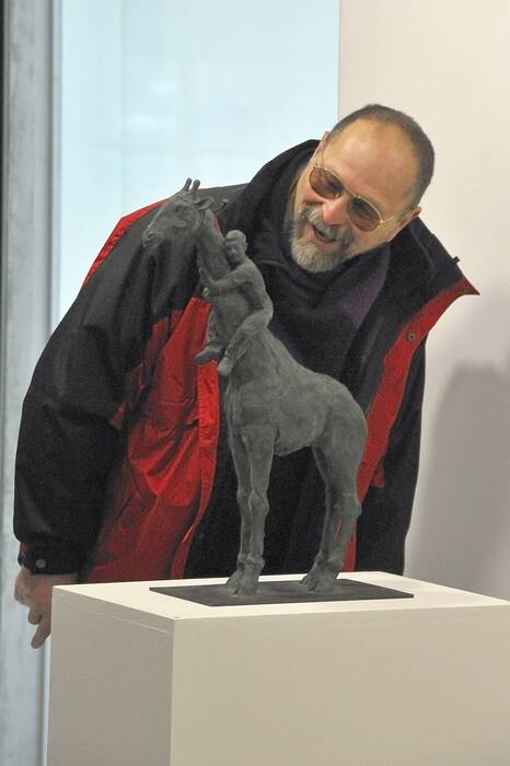  "Giraffe", 2000 von Stephan Balkenhol. Ausstellungsbesucher betrachtet lächelnd eine schwarze Bronzeskulptur in Form einer Giraffe. An ihrem Hals klammert sich eine kleine Figur.