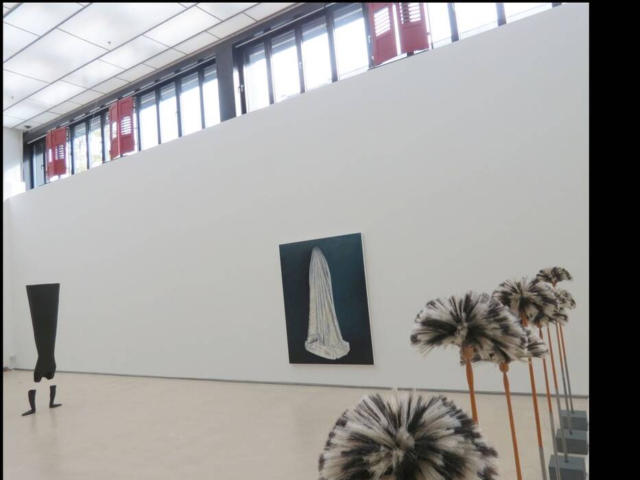 Ölgemälde "Damast" von Anja Luithle: Eine mit weißem Stoff verhüllte Person steht vor dunkelblauem Hintergrund. Im Vordergrund die kinetische Installation mit Ziegenhaarbesen. Links: "kopfüber", 2007. Ein schwarzes Kleid steht kopfüber im Raum.