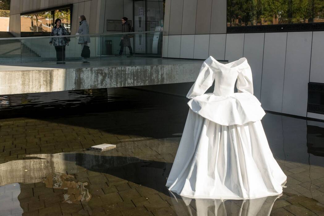 "Ein Vielleicht auf der Welle", 2014 von Anja Luithle. Schwimmende Skulptur GFK, Stahl, Lack. Eine weiße Robe steht im Wasser vor dem Stadthaus. Drei Bürgerinnen verlassen das Stadthaus.