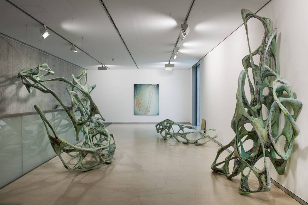 Drei pastellgrün-schwarze Skulpturen wirken wie biomorphe Gebilde. Vor Kopf ebenfalls ein Kunstwerk von Wolfgang Flad.