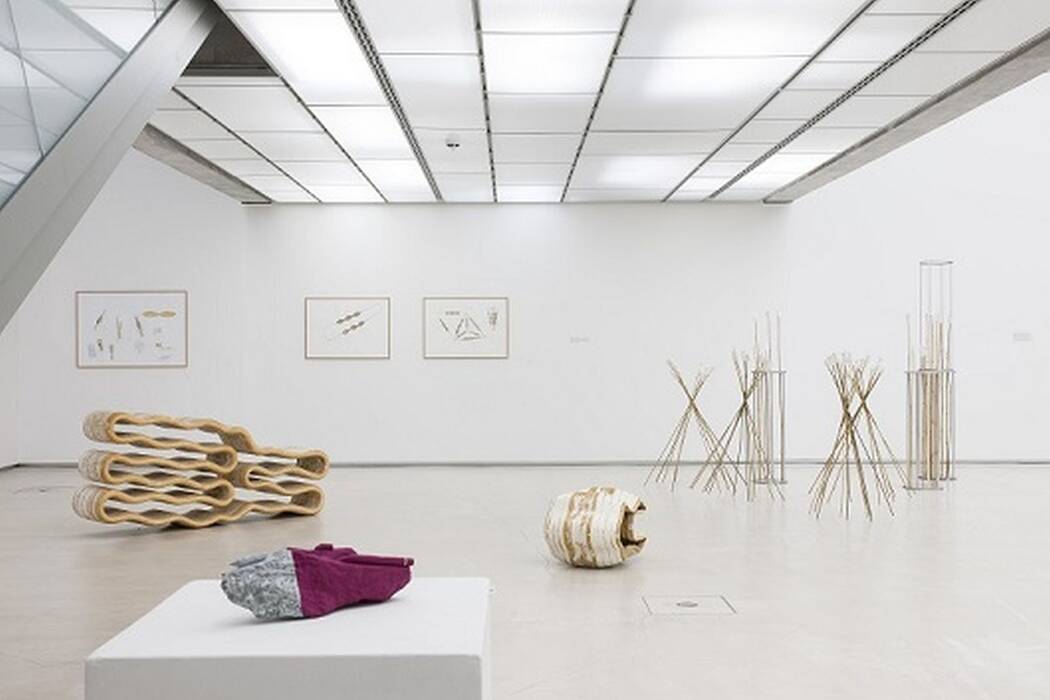 Ausstellungsansicht "ja natürlich",2016. Serie dreier minimalistischer Zeichnungen. Links eine wellenförmige Skulptur, rechts Kornähren-Objekte, davor ein Bodenobjekt in organischer Form. Im Vordergrund liegt auf einem Sockel ein Gebilde in Grau/Lila.