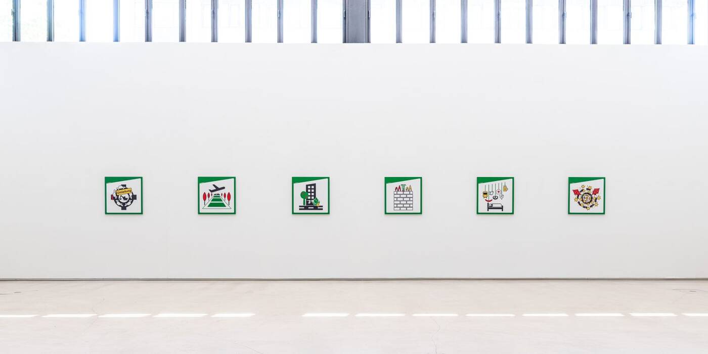 Ausstellung "City X - Ich, Ostfildern" - Doris Graf. An einer weißen Wand hängen sechs Piktogramme in den Farben Grün, Weiß, Grau, Rot, Gelb. 