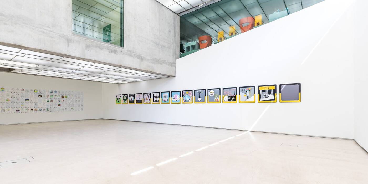 Raumansicht der Ausstellung "City X - Ich, Ostfildern" von Doris Graf. Zur linken Hand eine Wand voller selbstgemalter Bilder der Bürger. Rechts: Piktogramme mit gelb-schwarzem Rahmen.