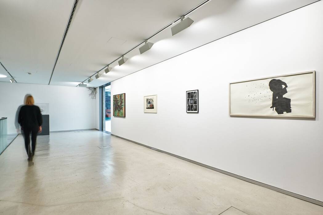 Ausstellung "Facetten": Oberer Galerieraum. Drei gerahmte Bilder und eine Leinwand. Eine Besucherin geht durch den Raum.