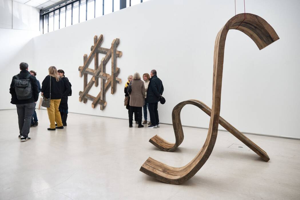 Ausstellungsbesucher mit Wandskulptur: „Big Cube“, div. gebrauchte Hölzer, ca. 280 x 280 x 3 cm, von Robert Steng. Zwei hölzerne, gebogene Raumobjekte,