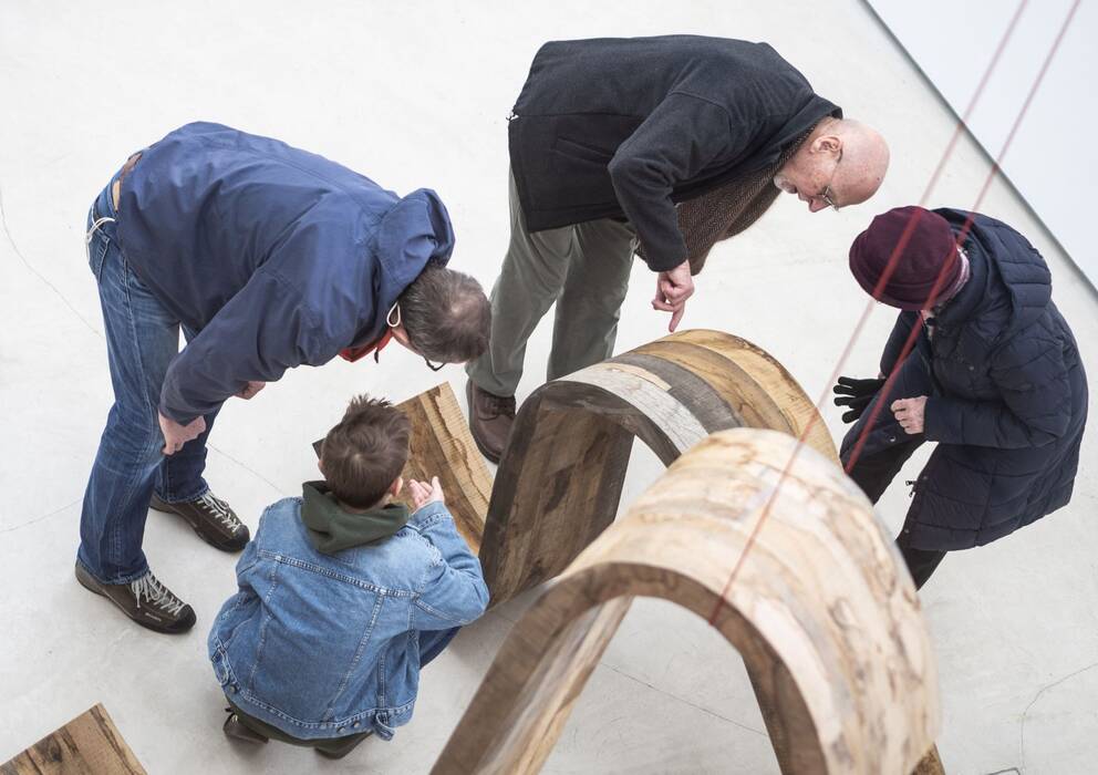 Vier Besucher hocken und stehen um zwei, geschwungene Bodenskulpturen von Robert Steng in der Ausstellung "Brettspiele", 2020.