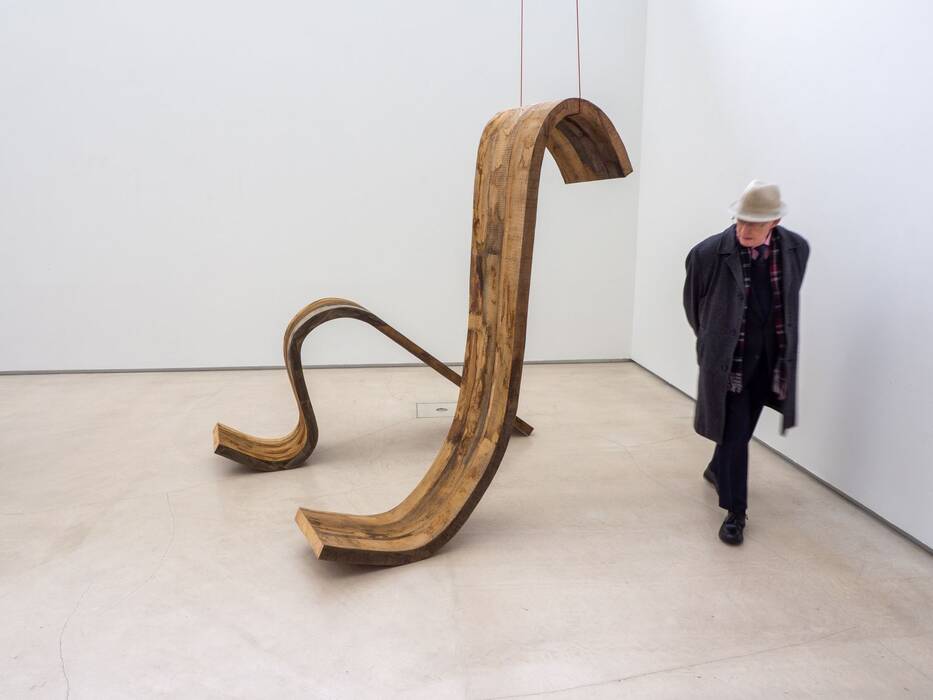 Ein Ausstellungsbesucher mit Hut und Mantel geht um Robert Stengs Bodenskulptur herum.