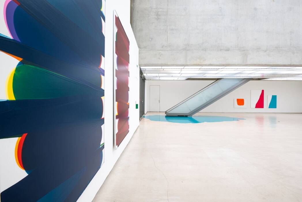 Ausstellung "nicht eintönig". Leinwände und Farbguss von Rainer Splitt. Im Hintergrund drei Exponante in grellen Farben.
