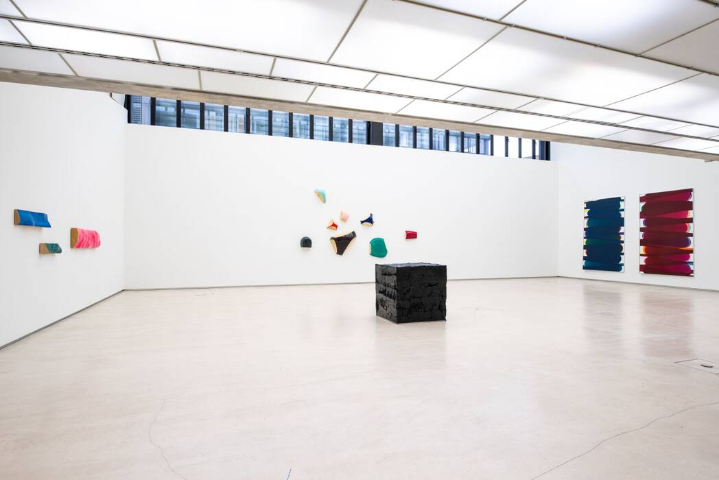 Ausstellungsansicht "nicht eintönig" mit Holder, Lutzeyer und Splitt. Links: Drei schmale Balken in Blau, Grün und Pink. Mitte: Wandarbeiten in Schwarz, Magenta, Blau - und Grüntönen. Rechts: Zwei Leinwände. In der Raummitte ein schwarzer Kubus.
