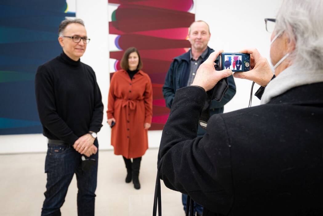Eine Besucherin fotografiert die Künstler mit der Galerieleiterin vor den Exponanten.