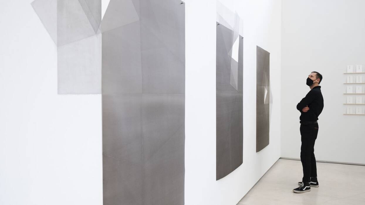 Ausstellungsbesucher vor der Serie "folding expanded positive on wall" von Michelin Kober. Großformatige Tuschezeichnungen in Grau bis Schwarz Nuancen, die sich auf der Wand fortsetzen.