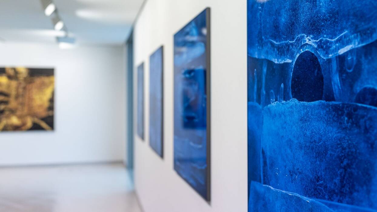 Eisblaue Fotoserie. Im Hintergrund hängt verschwommen ein Kunstwerk in Goldgelb und Schwarz.