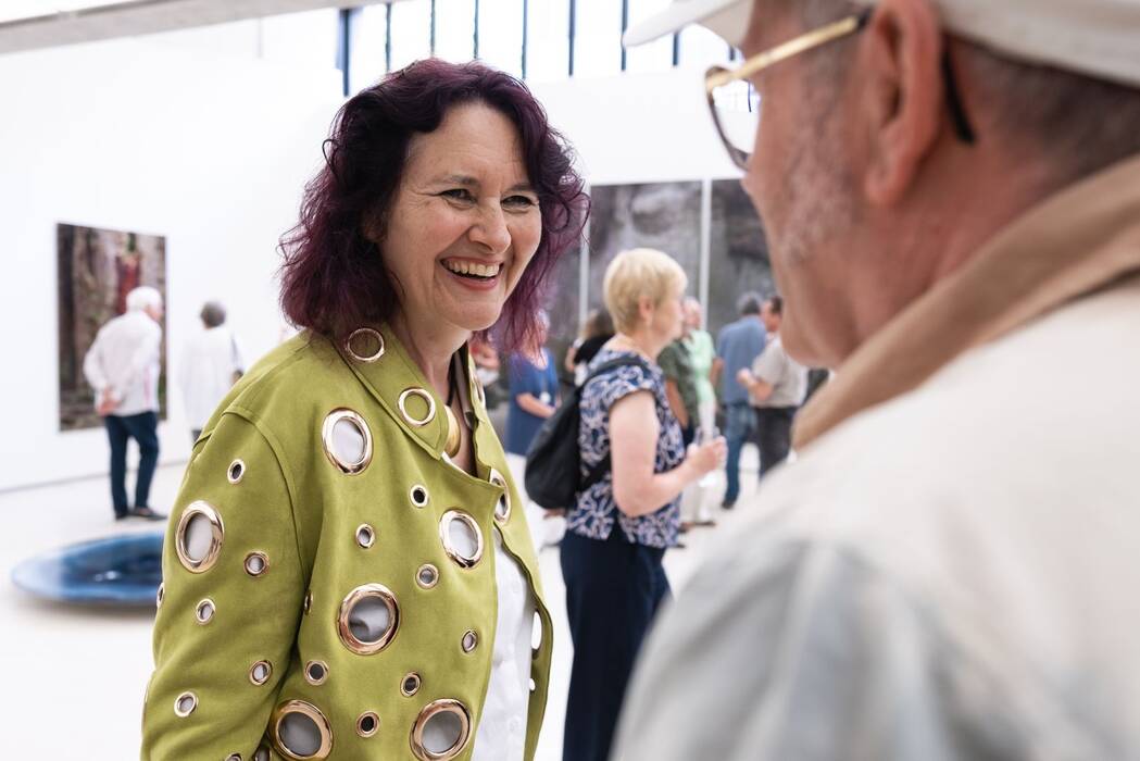Die Künstlerin Isabell Munck ist lachend im Gespräch mit einem Besucher. 