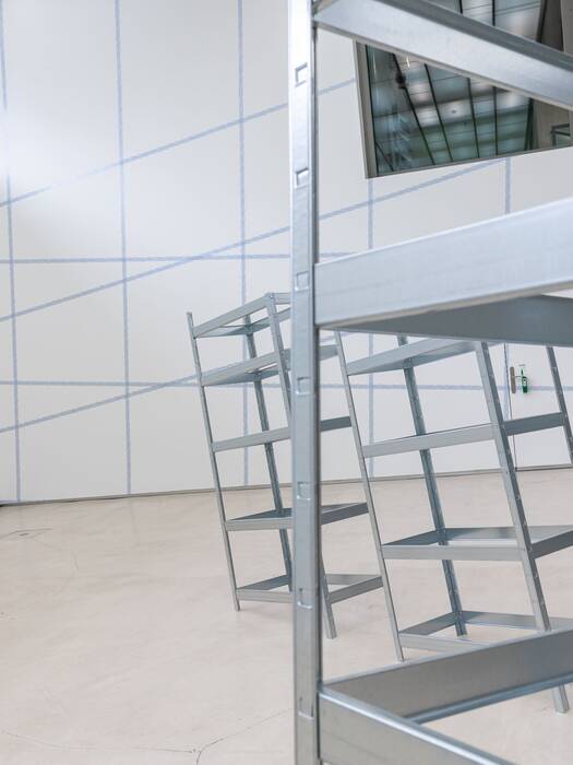 Installation mit Schwerlastregalen vor blaugerasterten Galeriewänden.