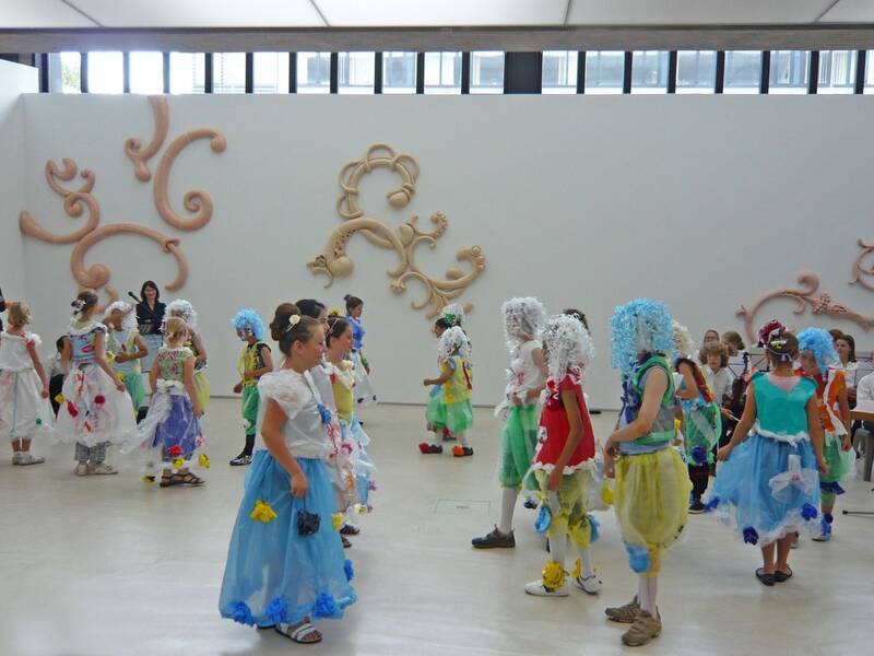 Ausstellung "Barock me" mit Gerold Tusch und Georg Winter, 2009. Aufführung vieler Kinder in barocker Kleidung mit Perücken. Im Hintergrund ein Streichorchester. An der Wand sind barocke Formen.